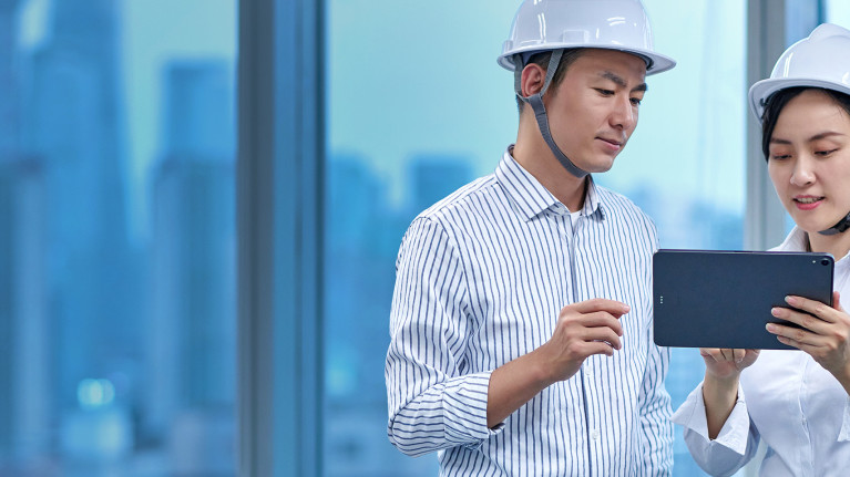 A man and a woman wearing safety helmets and using a tablet
